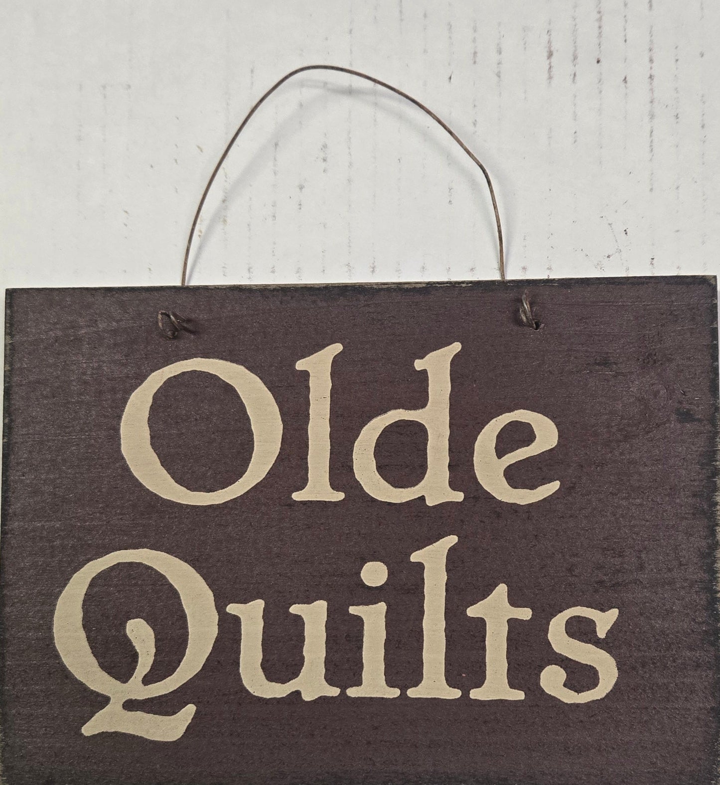 Wooden sign with 'Olde Quilts' text on a white background
