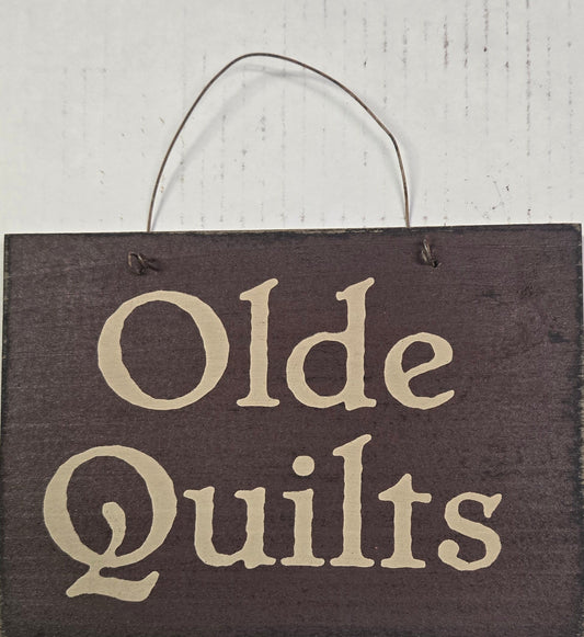 Wooden sign with 'Olde Quilts' text on a white background