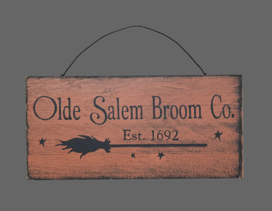 Wooden sign with 'Olde Salem Broom Co.' text and broom silhouette on a wooden background