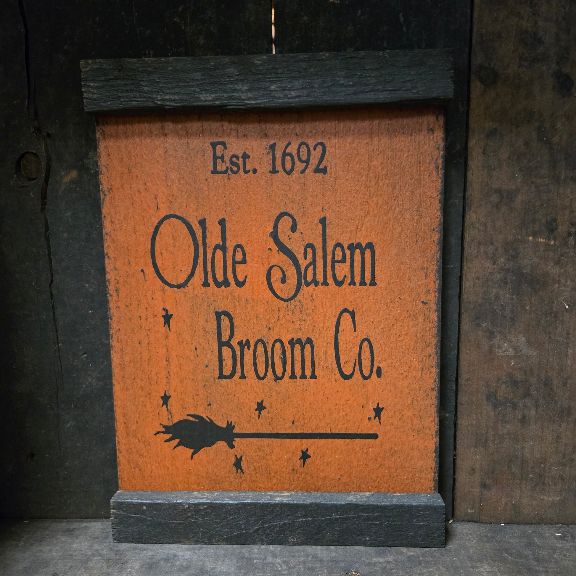 Wooden sign with 'Olde Salem Broom Co.' text and logo on a dark background