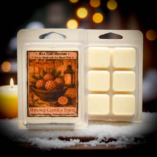 Wax tart melt package labeled 'Orange Clove & Spice' with a blurred candle in the background.