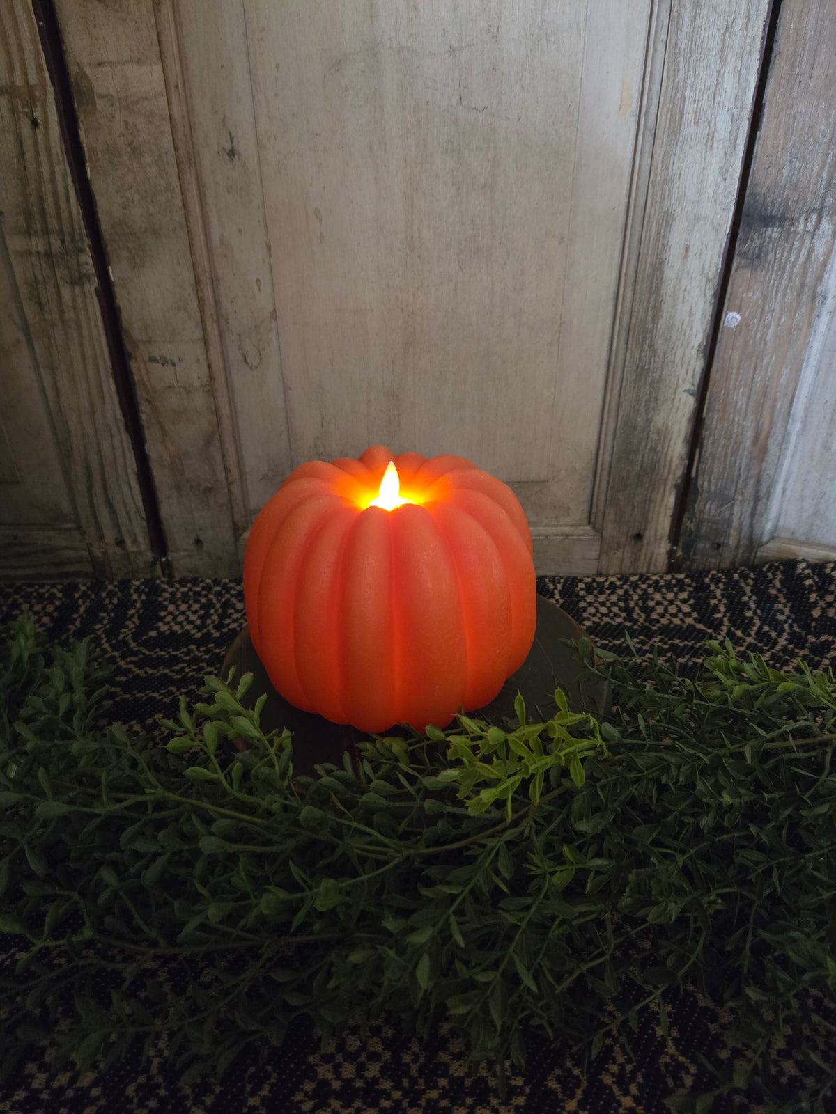Pumpkin candle with greenery in front of a weathered wood background.