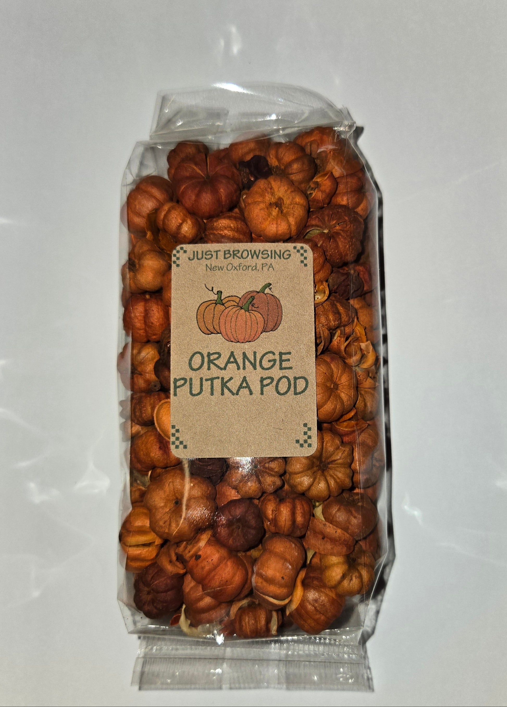 A clear plastic bag filled with dried orange-colored pod-like snacks or candies, with a kraft paper label reading 'JUST BROWSING ORANGE PUTKA POD'. The bag is photographed from above on a white sheet of paper over a speckled gray countertop.