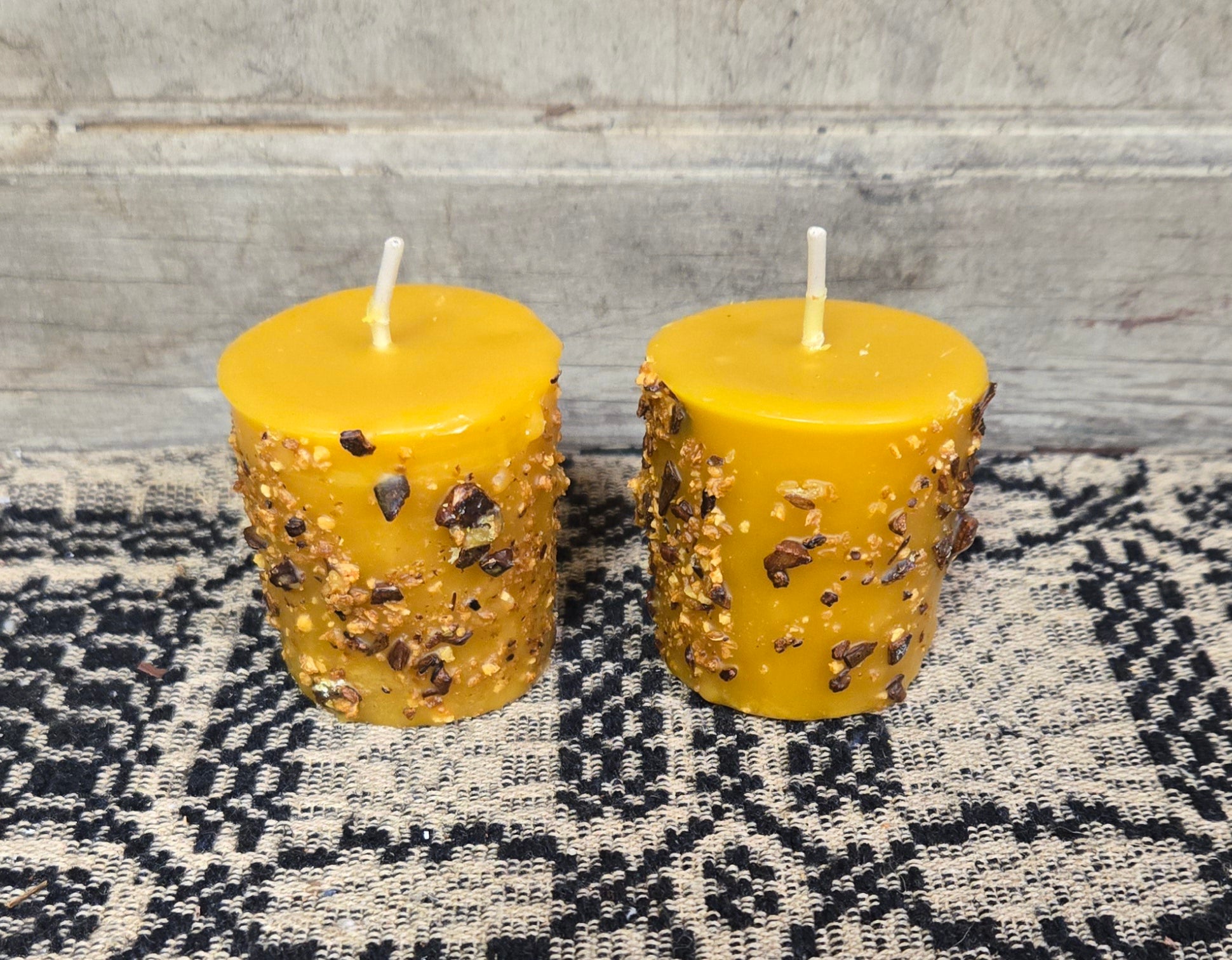 Two orange spice scented votive candles placed on a black and white patterned surface.