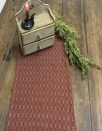 Red patterned table runner on a wooden table with a small wooden box and candle.