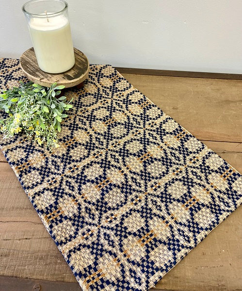 A navy and mustard geometric patterned table runner displayed on a wooden table with a candle and floral decor.