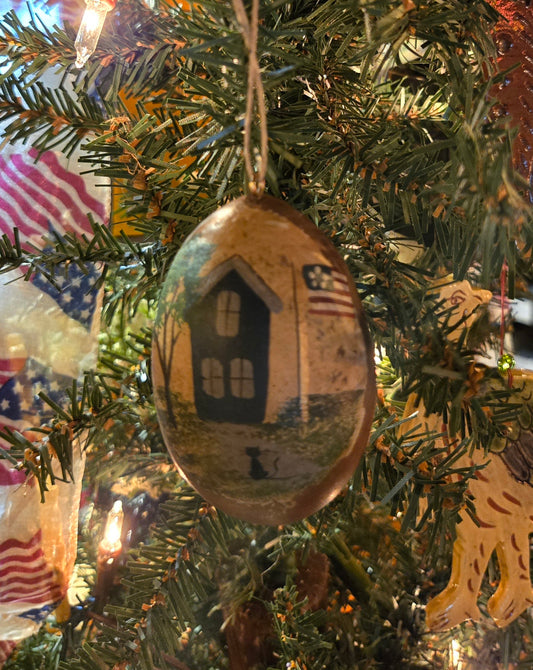 Handcrafted gourd ornament with a depiction of a house and a cat, featuring an American flag, designed for use as holiday decoration.