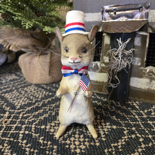 A hand sculpted paper mache mouse figurine wearing a patriotic red, white, and blue bow tie and a top hat with a similar design.