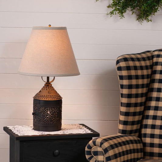Table lamp with decorative base on a nightstand next to a plaid chair against a white paneled wall.