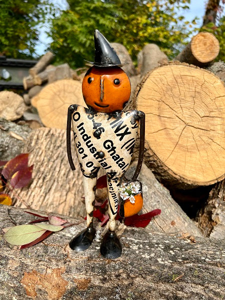 Metal pumpkin man standing in front of logs