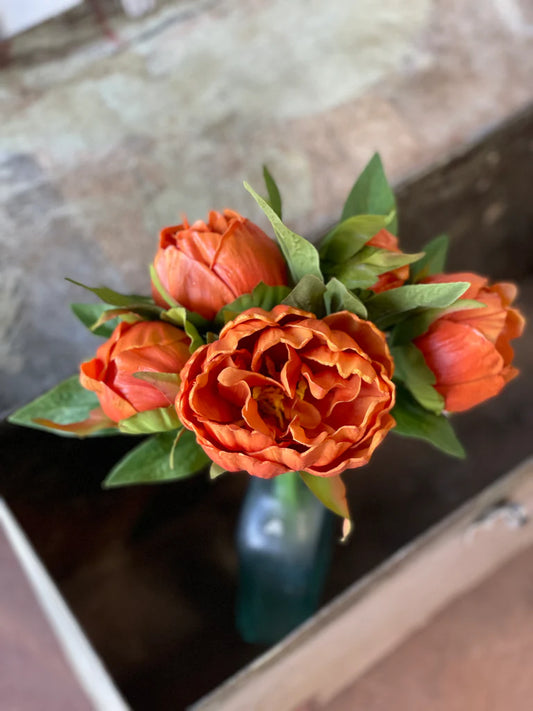 A bundle of artificial peony flowers tied with raffia, with a vibrant orange and pink color palette, displayed in front of a plain background.