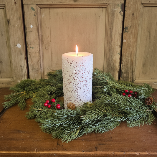 White candle with a wooden base and greenery on a wooden surface