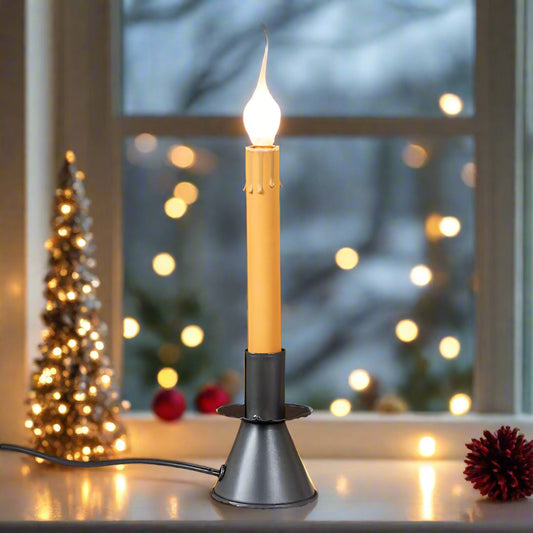 An electric window candle with a classic cone candlestick base in a smokey black finish, emitting a warm light, placed on a windowsill.