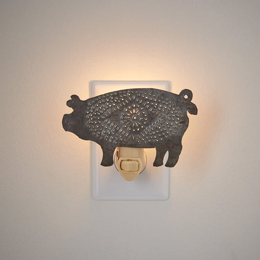 Punched pig night light in tin plugged into a wall outlet on tan background