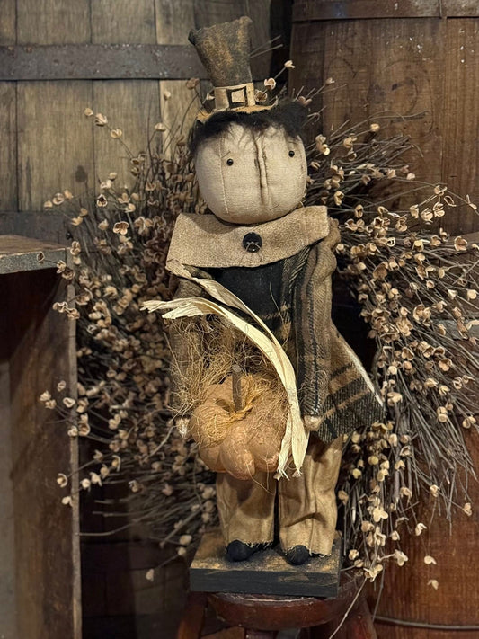 Decorative figure of a pumpkin with a top hat and scarf, surrounded by dried plants on a wooden surface.
