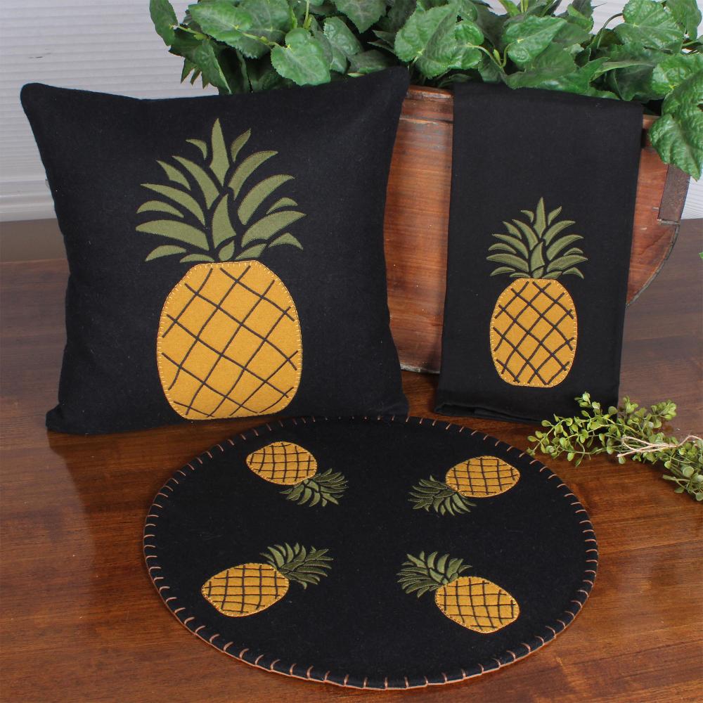Black pillows and round mat with pineapple designs on a wooden surface.