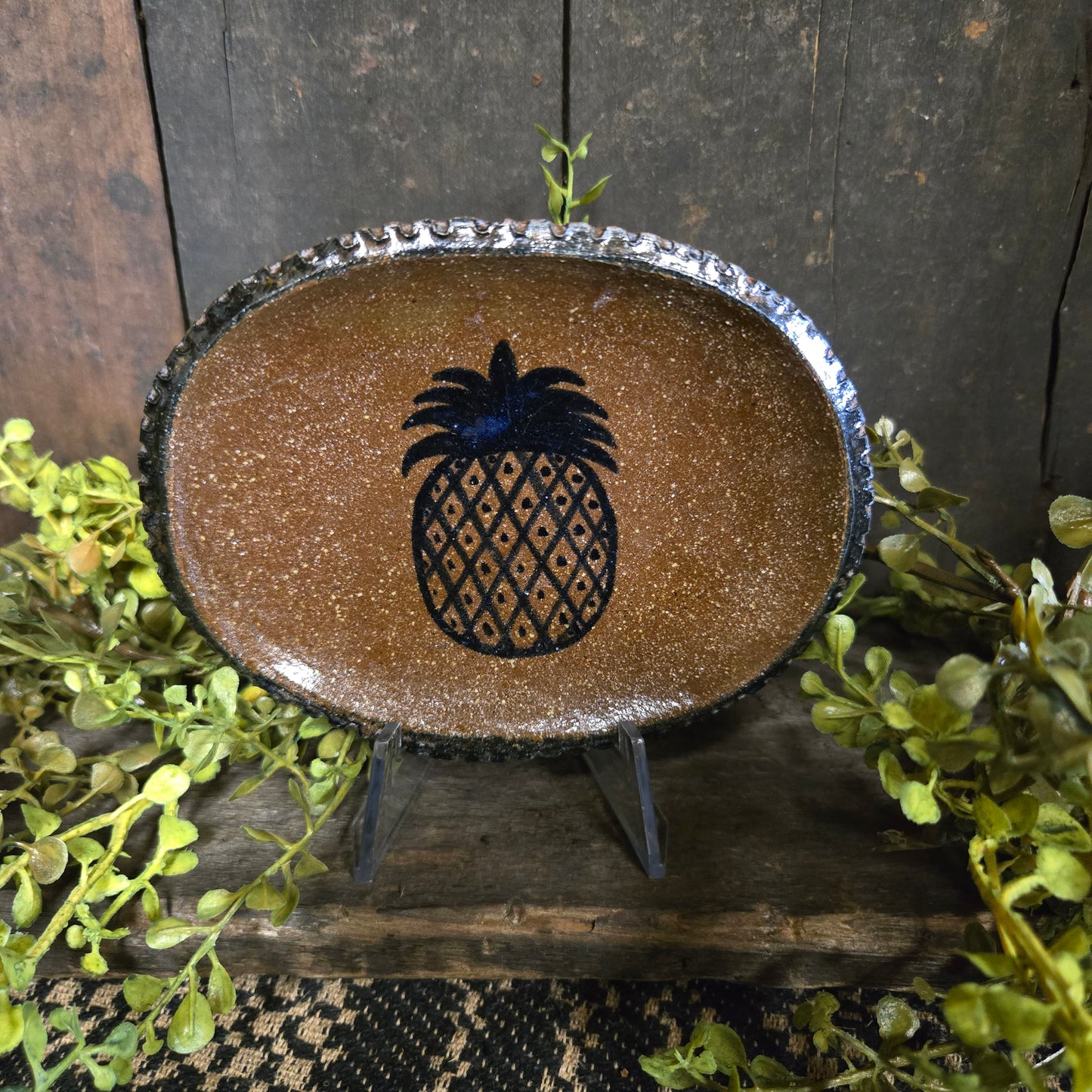 Brown ceramic dish with black pineapple design on a wooden surface with greenery