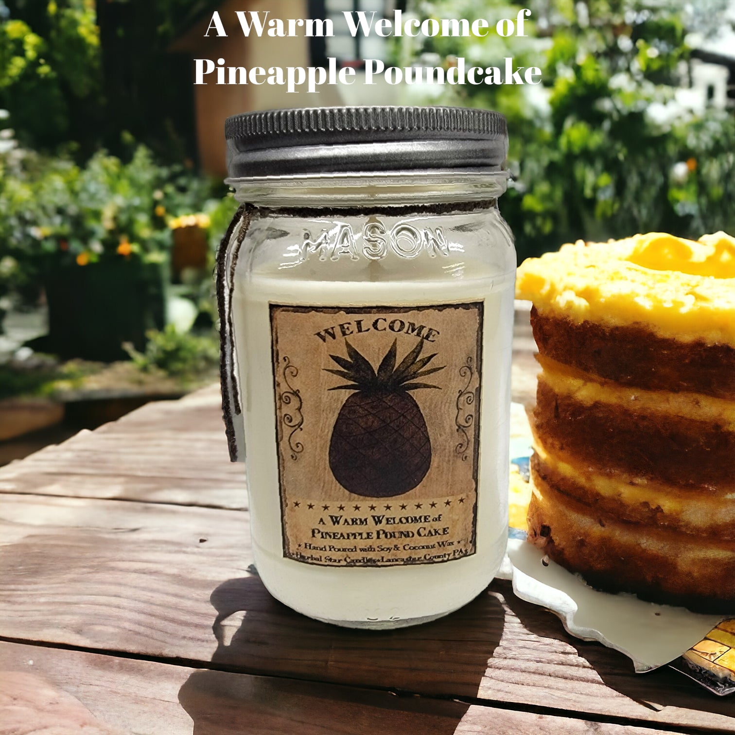A mason jar candle with a label that reads 'Welcome' and depicts a pineapple, placed on a wooden surface with a cake in the background.