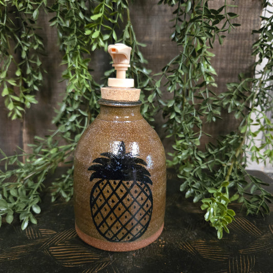 Decorative bottle with pineapple design on a wooden surface with greenery