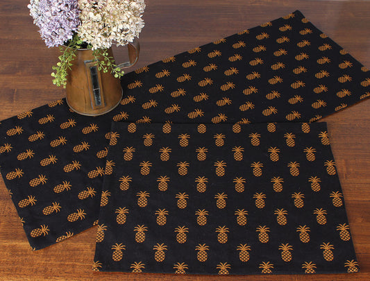 Black placemat with mustard color pineapples on wooden table with flowers in vase