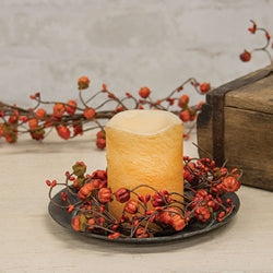 A decorative candle ring with flexible stems wrapped in brown material, adorned with orange pip berries, miniature orange pumpkins, and light green leaves, displayed around a candle.