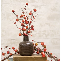 A decorative berry pick with orange pip berries, miniature orange pumpkins, and green leaves, arranged in a vase with a plain background.