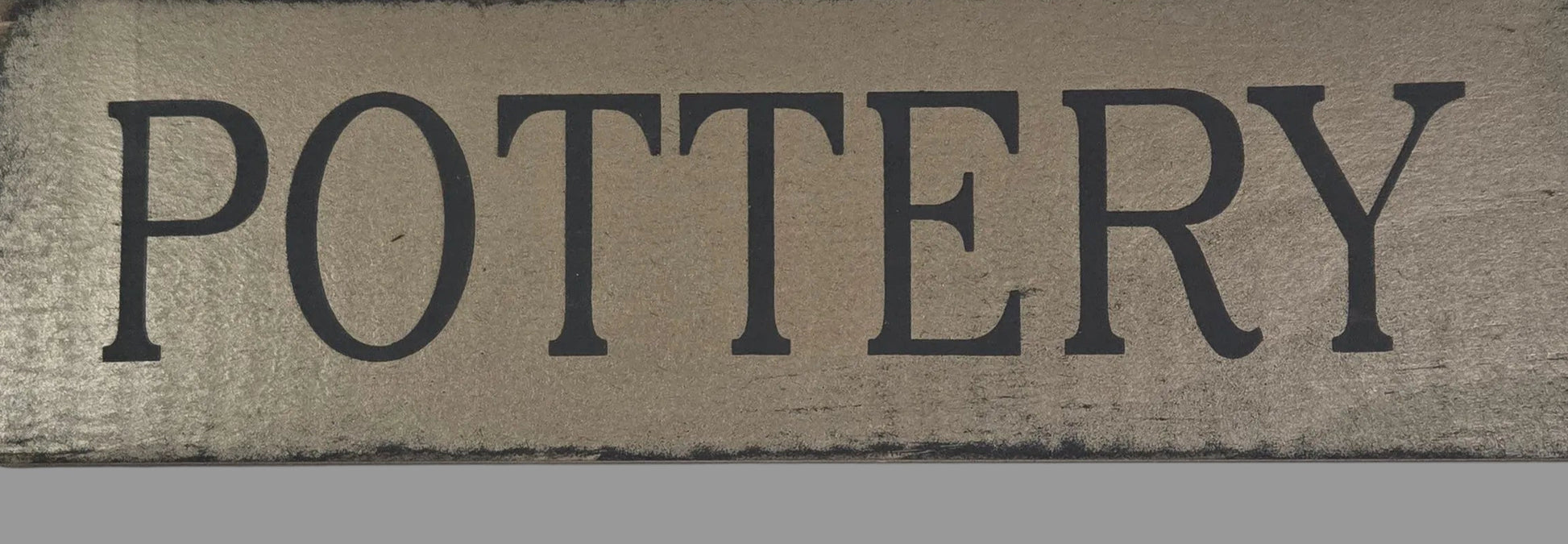 Wooden sign with 'POTTERY' text on a gray background