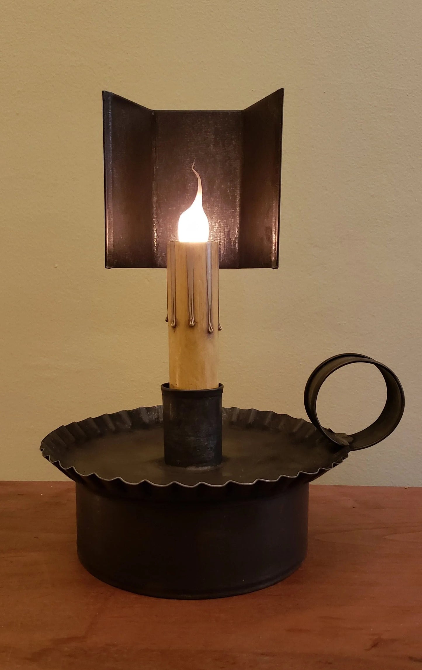A black Prairie Tin Accent Light with a lit candle, placed on a wooden surface.