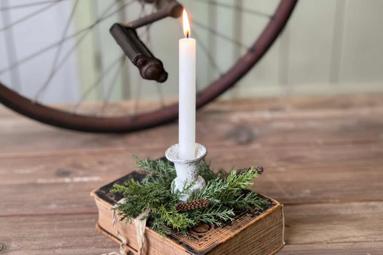 Candle in a decorative holder on top of an old book with greenery, against a rustic background.