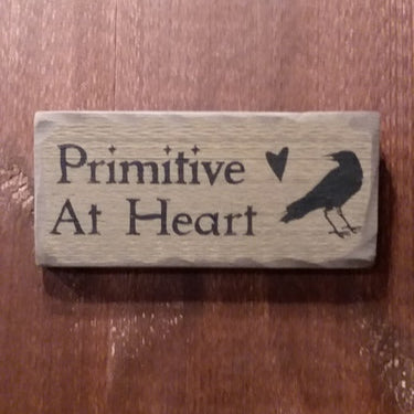 Worn sign with a the words "Primitive At Heart" with a crow and heart