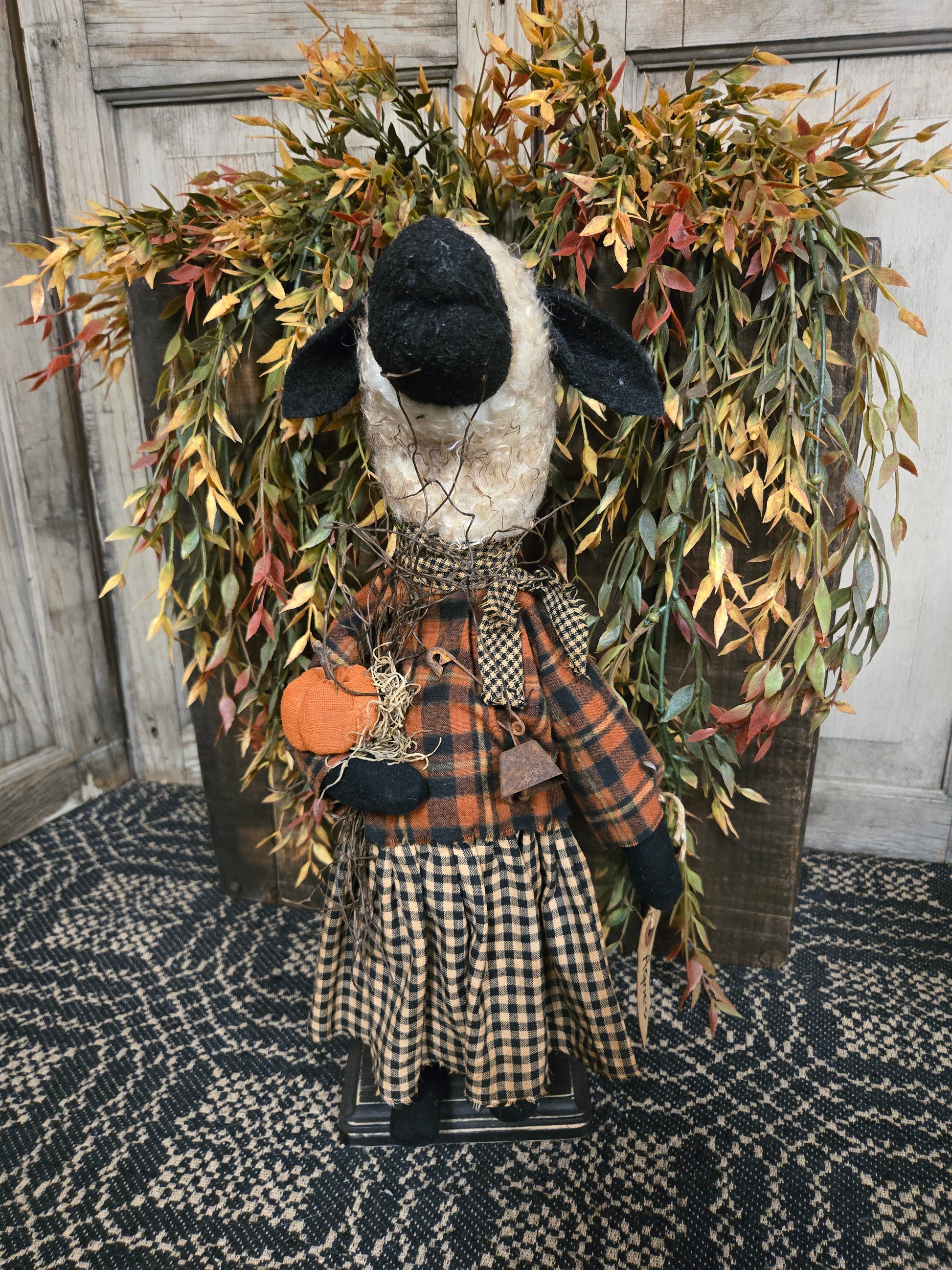 Decorative wreath with a black and white sheep figure, plaid fabric, and autumn leaves on a textured surface.