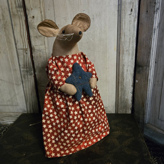 Small mouse figure wearing a red and white star-patterned dress on a wooden surface