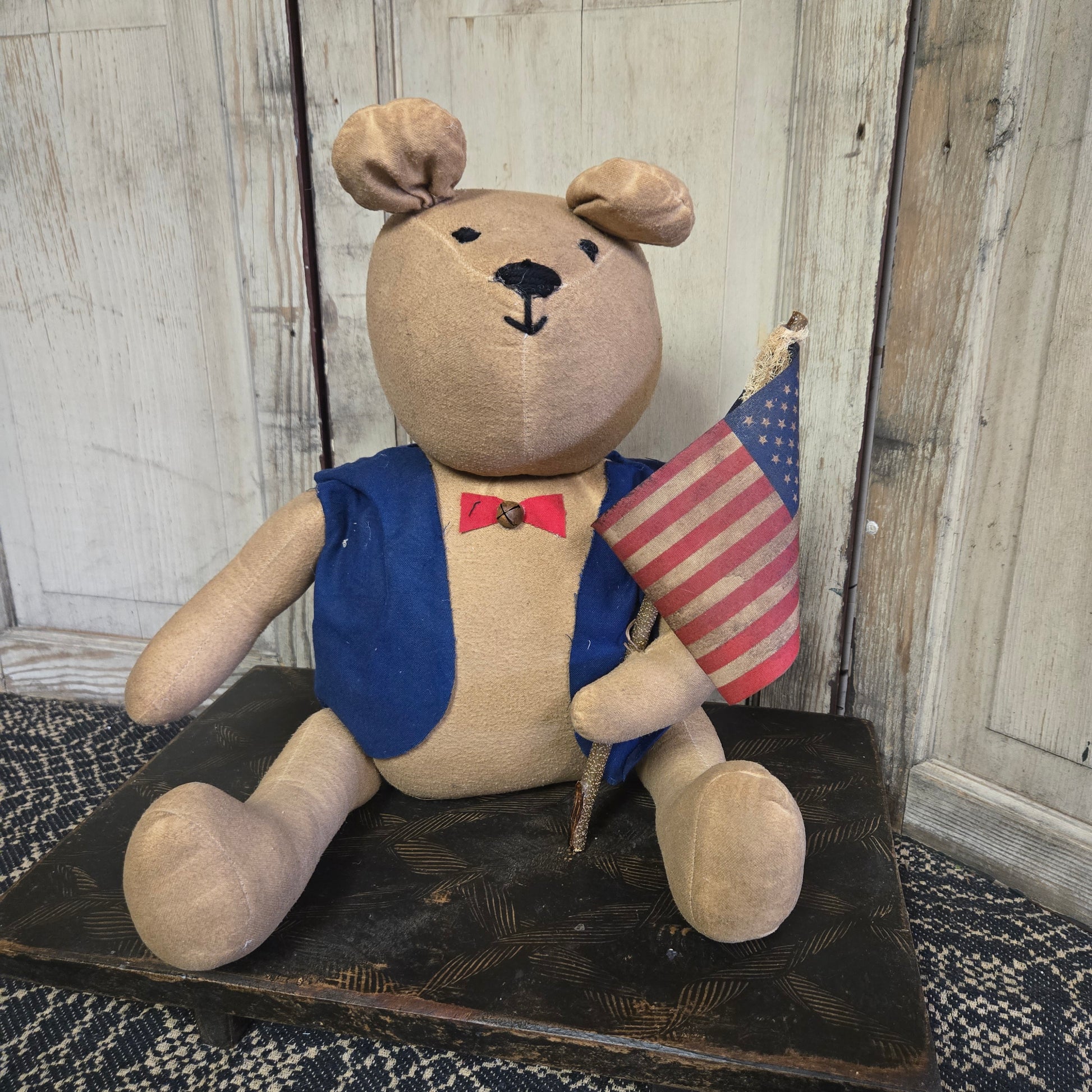A teddy bear with a patriotic design, holding an American flag, wearing a blue jacket and a bow tie.