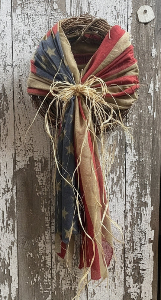 Grapevine wreath with flag draping on a rustic wood background.
