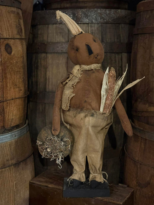 Scarecrow figure with a pumpkin head in a rustic setting with wooden barrels.