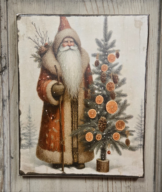 A canvas print depicting a traditional, primitive design of a bearded man dressed as a Santa Claus figure standing next to a decorated Christmas tree, with snow on the ground and a winter landscape in the background.