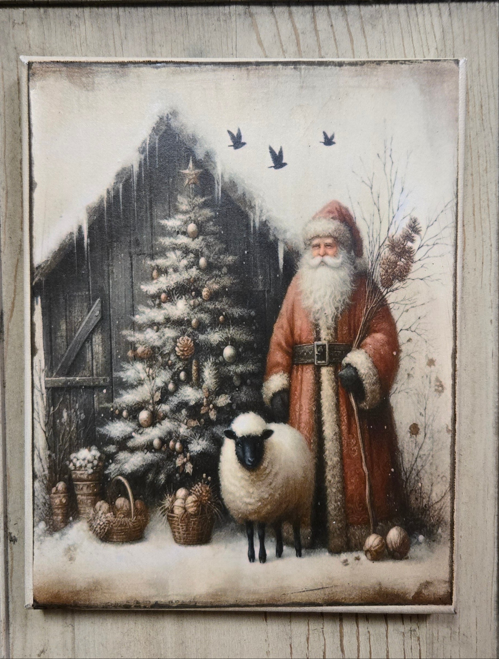 A canvas print depicting a traditional, primitive design of Santa Claus standing next to a sheep with a Christmas tree and a rustic cabin in the background.