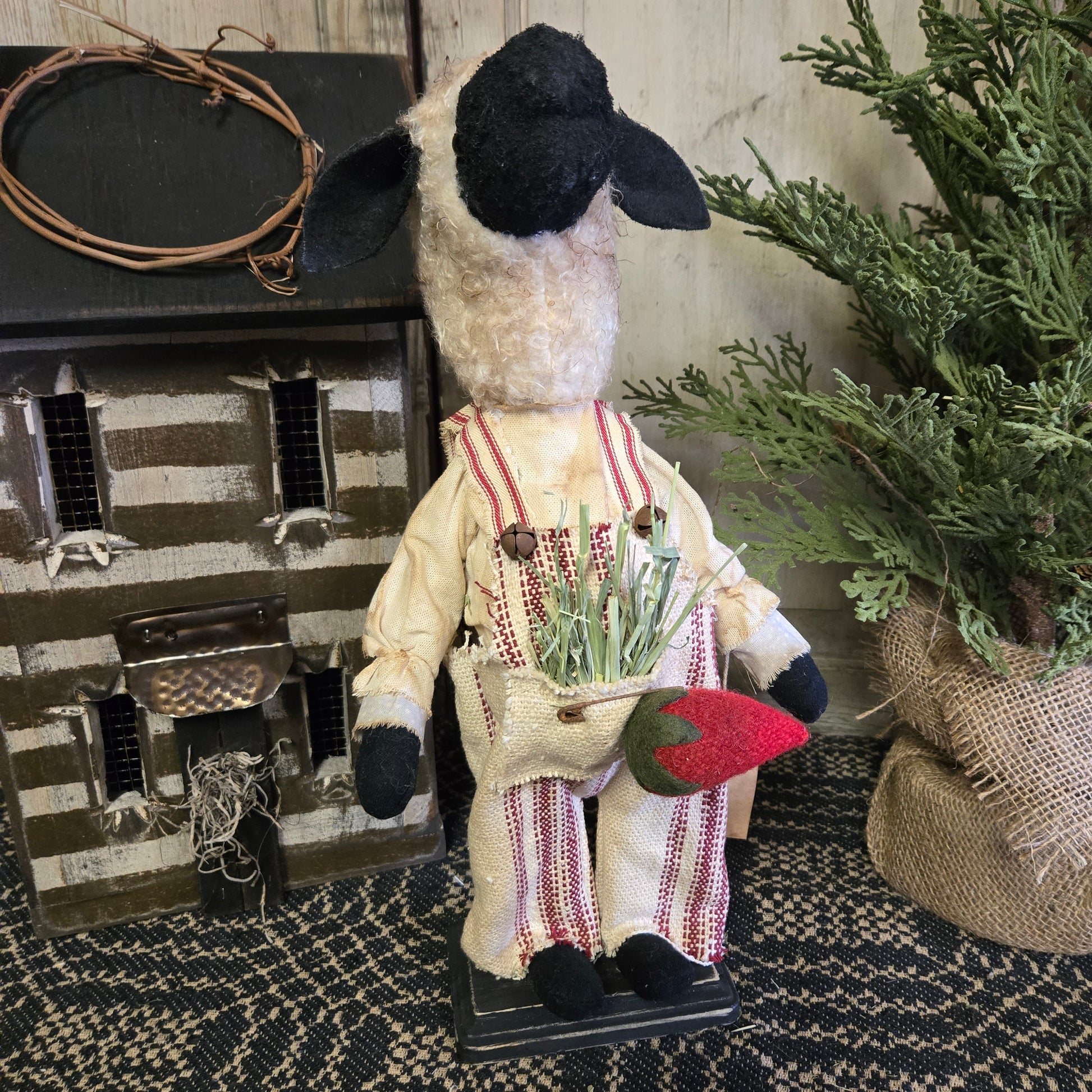 A decorative figurine of a sheep wearing a outfit with stripes and holding a red heart, positioned on a surface with a rustic background.
