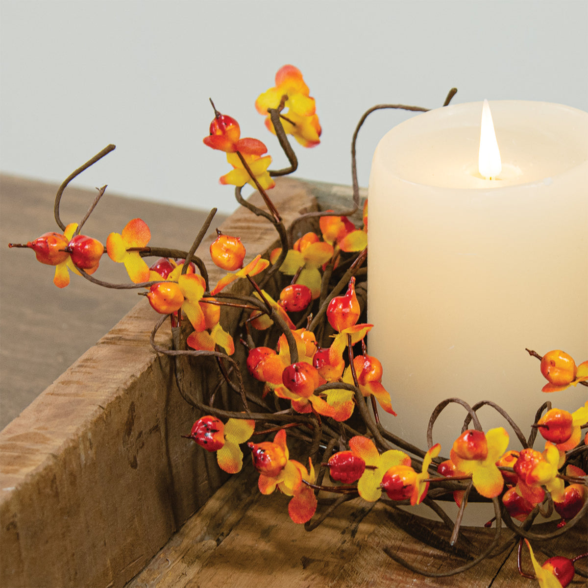 Decorative floral arrangement with red and yellow flowers around a lit candle on a stone surface.