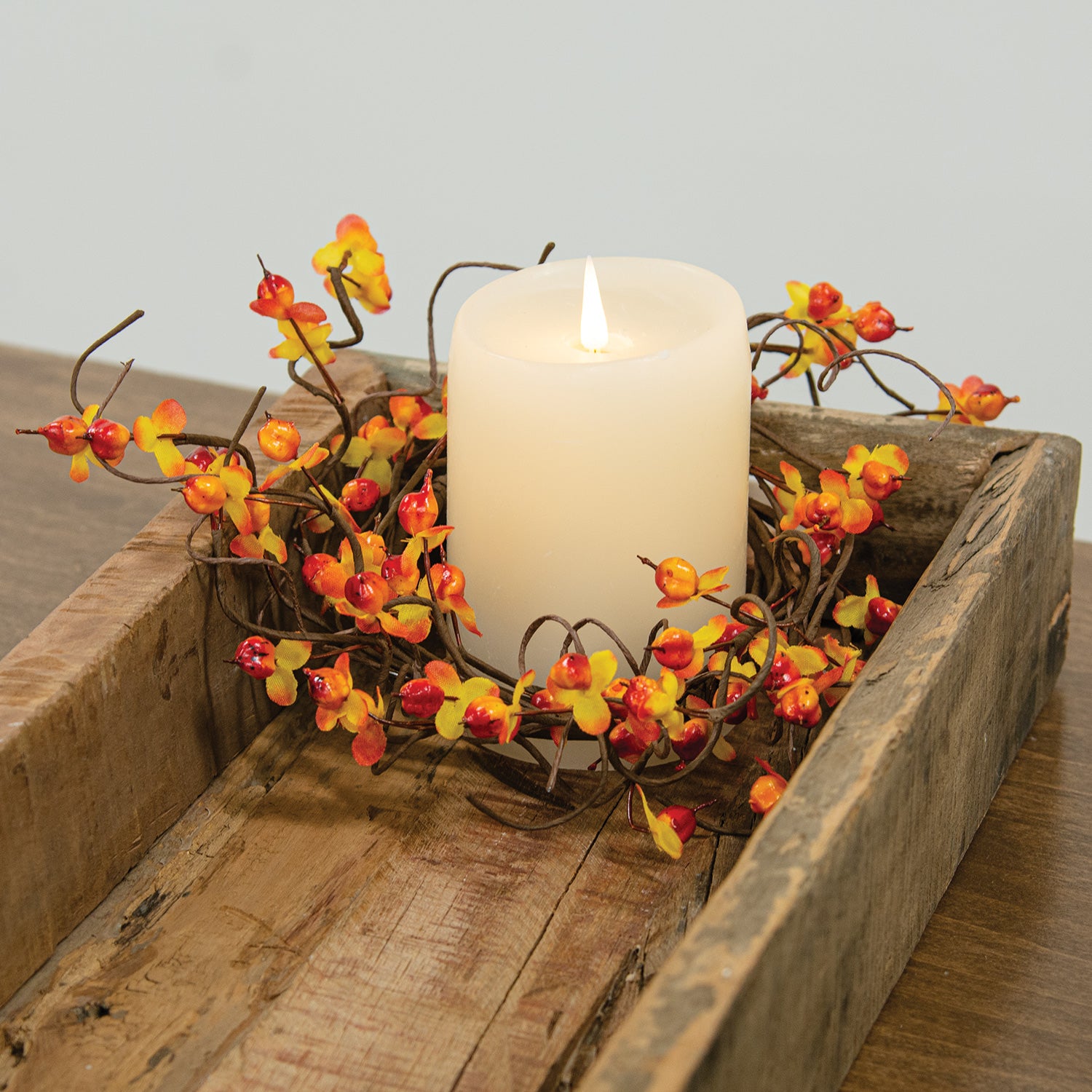 Candle in a wooden box with decorative branches on a wooden surface