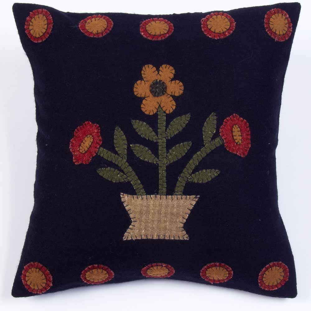 A black pillow with a floral embroidery design, featuring a stylized sunflower and other blooms in a geometric arrangement, set against a plain background.