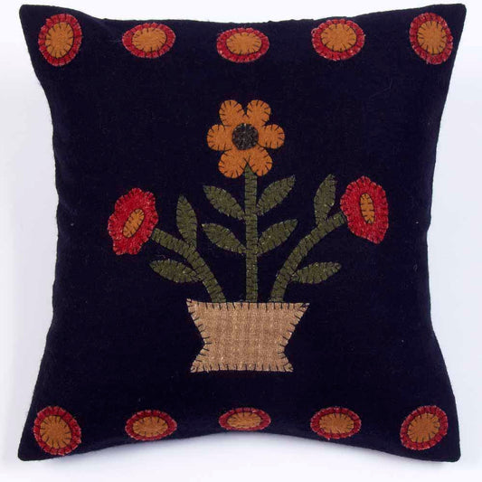 A black pillow with a floral embroidery design, featuring a stylized sunflower and other blooms in a geometric arrangement, set against a plain background.
