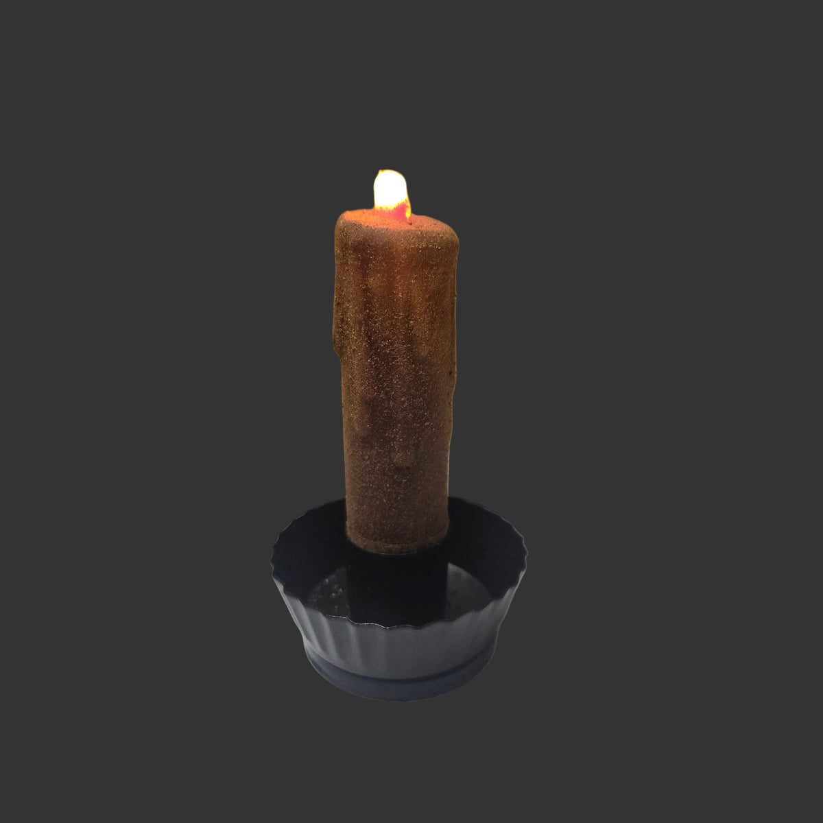 A single brown wax candle with a small white flame, standing upright in a black cup holder against a dark gray background.