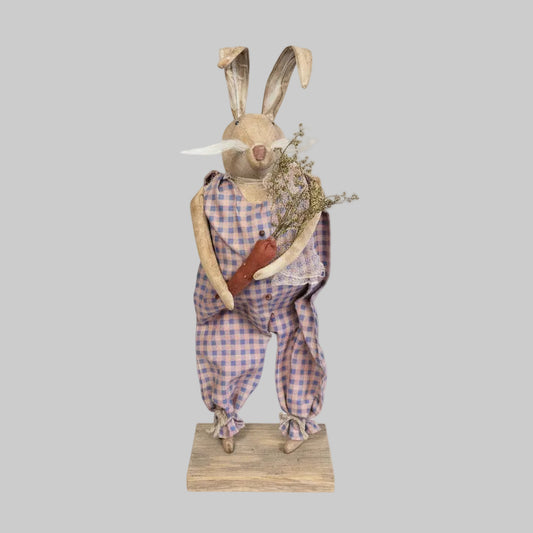 Decorative rabbit figure in checkered overalls holding a bundle of flowers on a white background
