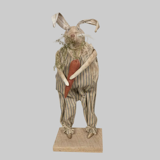 Decorative figure of a rabbit in striped overalls holding a carrot on a white background