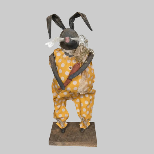 Decorative figure of a bunny wearing a yellow polka dot outfit on a wooden surface.