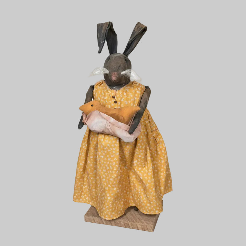 Bunny in a yellow dress with polka dots standing in front of a wooden door.