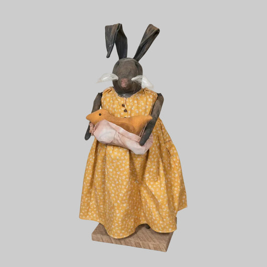 Bunny in a yellow dress with polka dots standing in front of a wooden door.