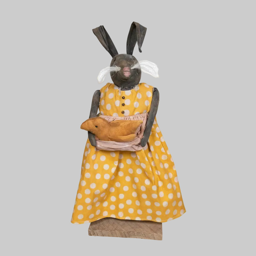 Vintage doll with yellow polka dot dress and brown shoes against a wooden wall.