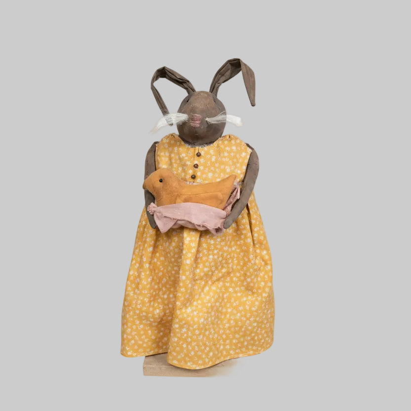 Stuffed animal in a yellow dress with a floral pattern on a wooden surface.